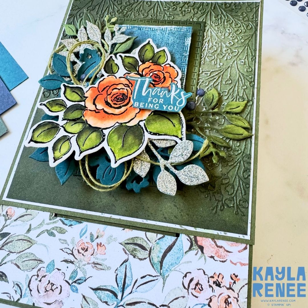 Close-up view of the card front from the pop-up drawer project, highlighting the layered die-cut roses, glittery silver leaves, and embossed textured background. The sentiment ‘Thanks for being you’ is centered among the foliage, framed by floral patterned paper at the bottom.