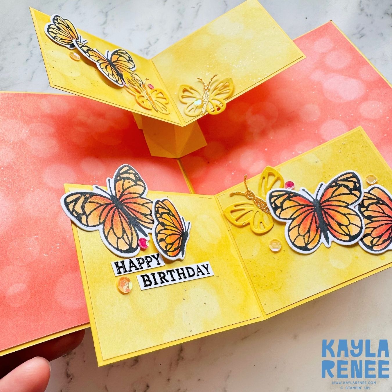 Close-up angled view of the fun fold birthday card, showing three-dimensional yellow and orange butterflies, glitter accents, and the 'Happy Birthday' sentiment on layered yellow panels.
