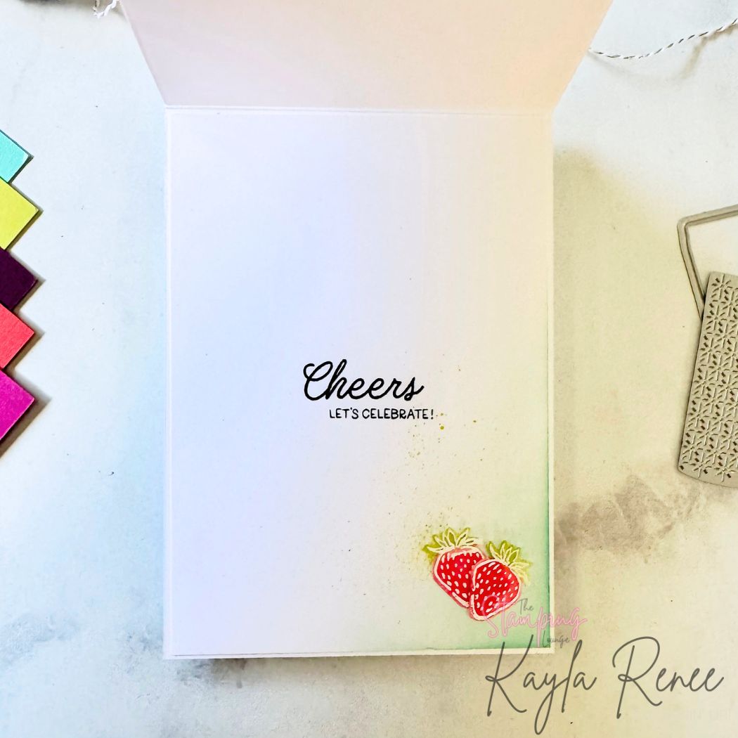 Inside of the card with a simple clean layout. The sentiment “Cheers — let’s celebrate!” is stamped in black. In the bottom corner are two small hand-stamped strawberries with subtle watercolour shading and background ink blending.