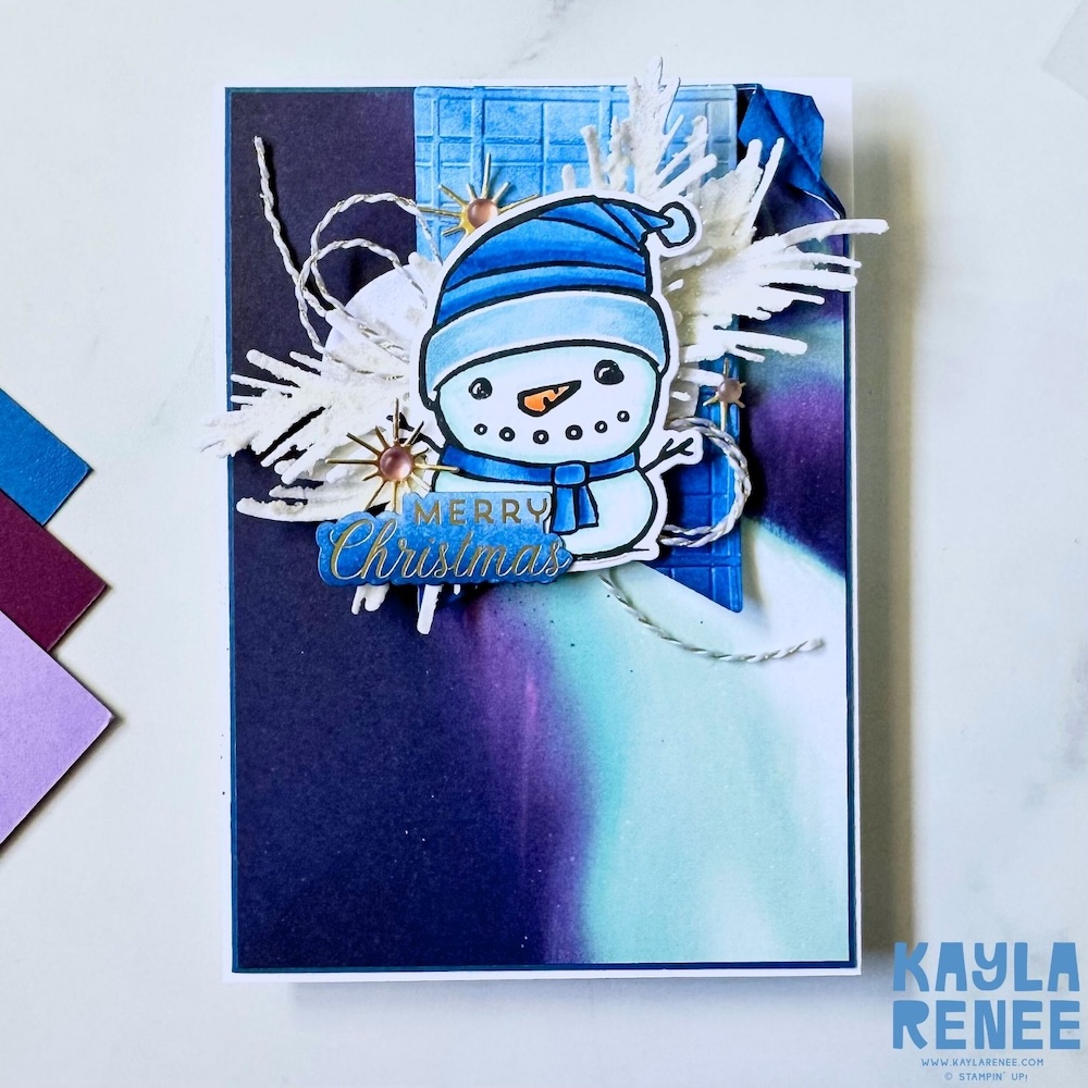 Handmade snowman Christmas card created with the Stampin’ Up! Festive Friends bundle, featuring a blue and purple blended background, white foliage accents and a Merry Christmas sentiment.