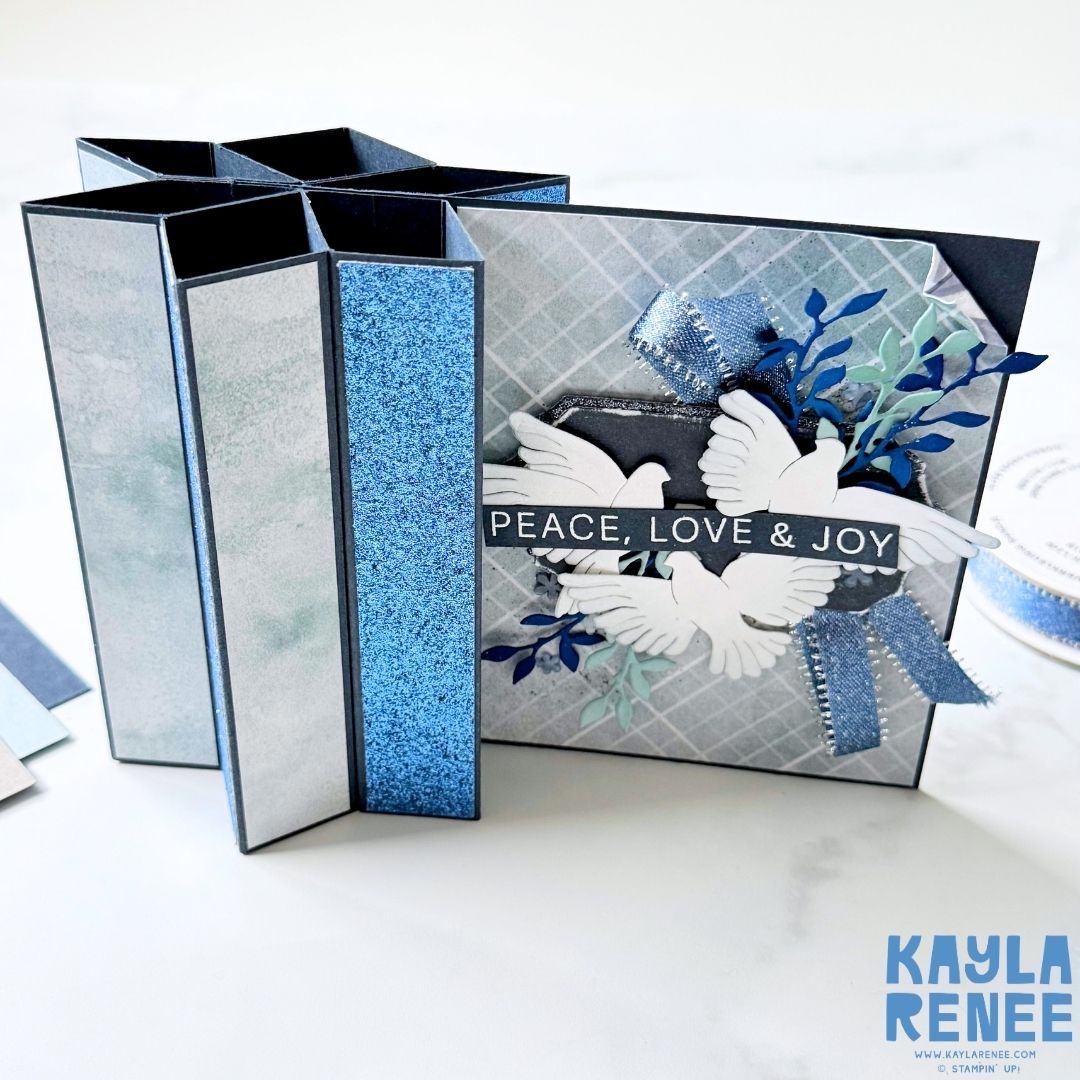 Close-up of a handmade star fun fold card by Kayla Renee showcasing the Peaceful Gardens suite. Decorated with glimmer blue panels, textured gray background, and layered die-cut doves with the sentiment “Peace, Love & Joy.”