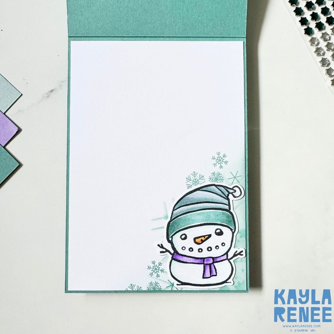 Inside of handmade Christmas card with a coloured snowman and a background of softy stamped snowflakes