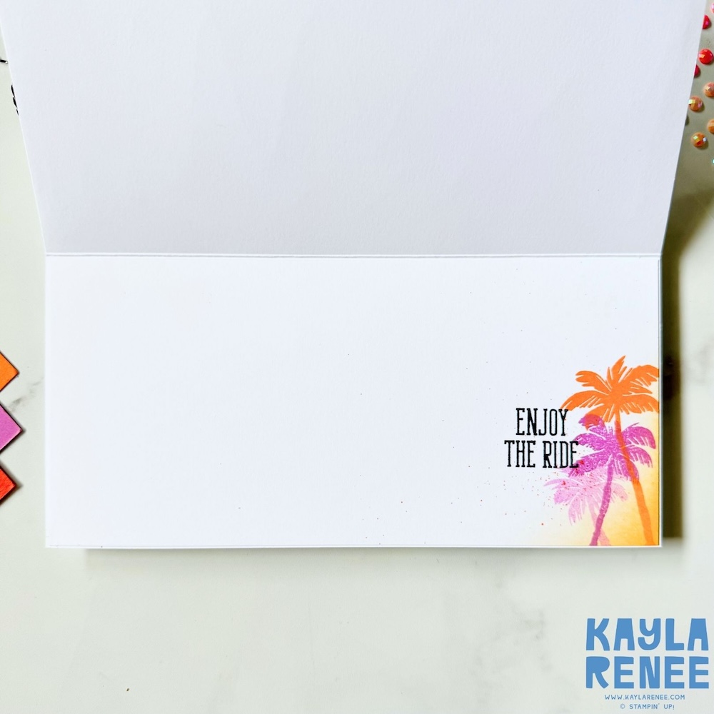 Inside view of a handmade New Year card with a clean white writing panel and a small stamped palm tree design in pink and orange ink with the sentiment “Enjoy the ride” in the bottom corner.