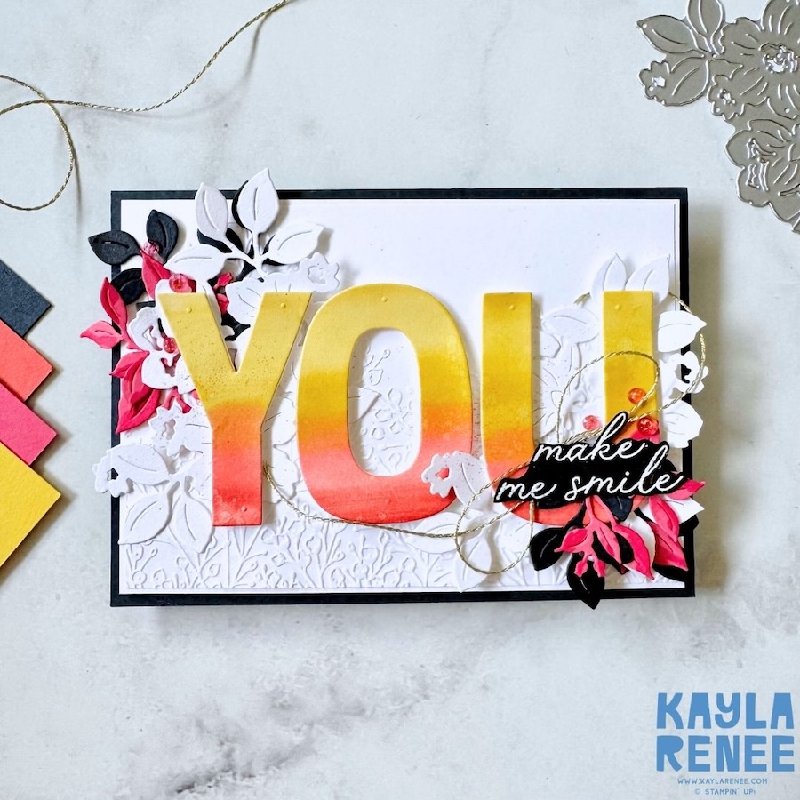 Close-up of the ombré “YOU” letters made with Stampin’ Up! Party Alphabet dies, showing soft ink blending and water-splatter texture. Layered die-cut florals and a black “make me smile” sentiment from the Charming Day bundle add dimension and contrast.