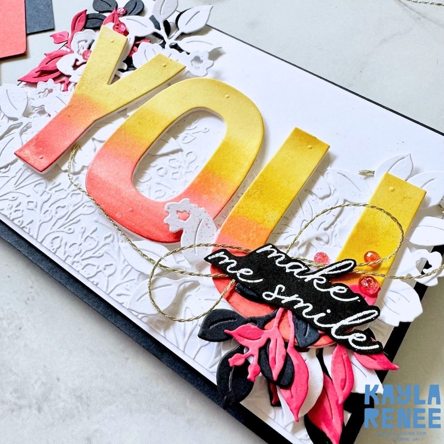 Angled detail of layered white, black, and pink die-cut flowers surrounding the Party Alphabet “YOU” letters, accented with gold thread and small embellishments using Stampin’ Up! Charming Day bundle elements.