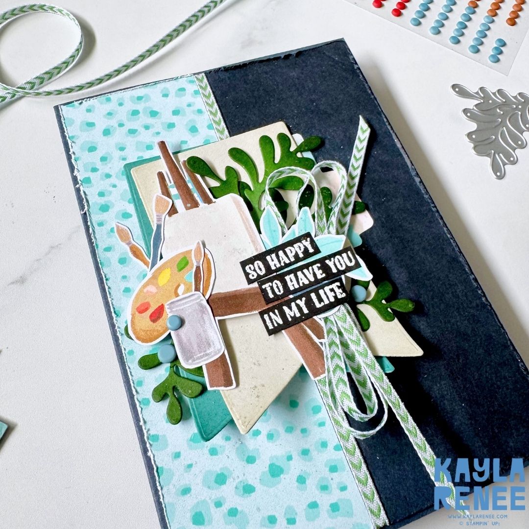 Close-up of a handmade Stampin’ Up! Hobby Haven card showcasing layered art and hobby embellishments, textured cardstock, leafy die cuts, ribbon detail, and a bold black sentiment strip.
