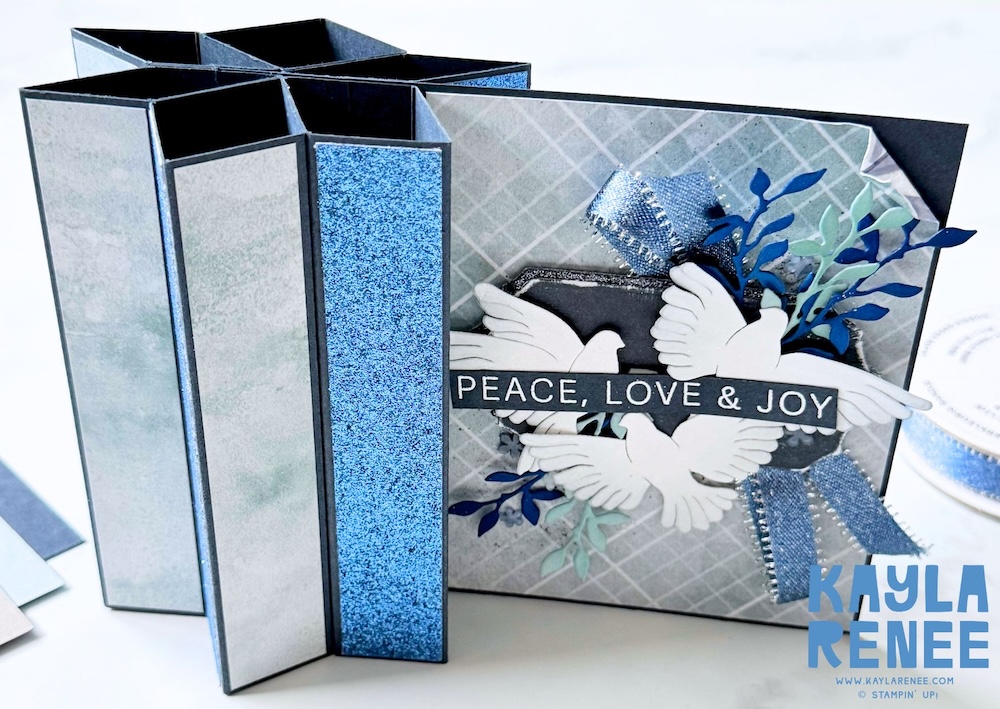 Handmade star fun fold Christmas card created by Kayla Renee using the Stampin’ Up! Peaceful Gardens suite. Features layered white doves, blue glimmer paper, and the sentiment “Peace, Love & Joy” with silver and denim blue ribbon accents.