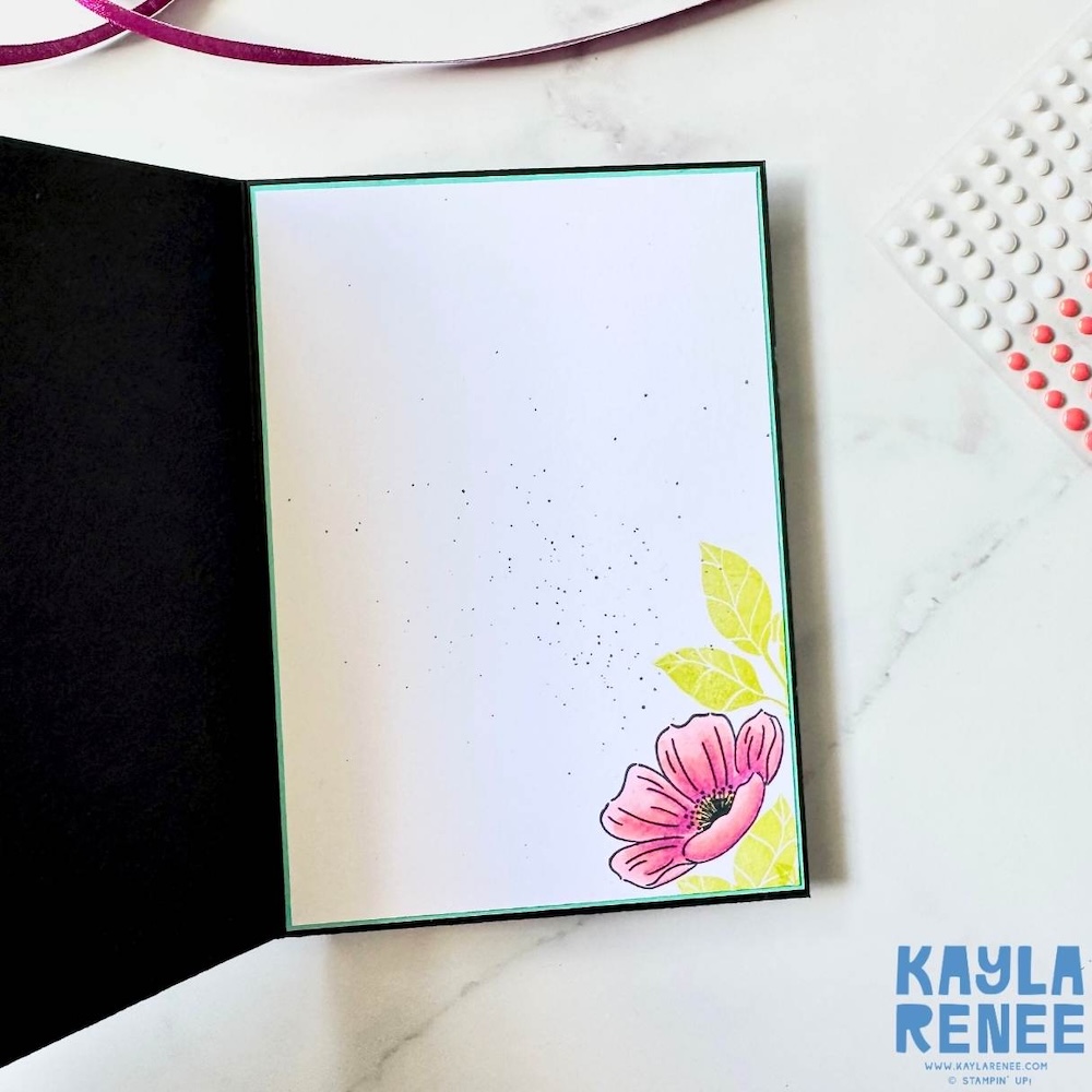Inside view of handmade greeting card showing clean white writing panel with stamped floral corner detail and ink splatter accents.