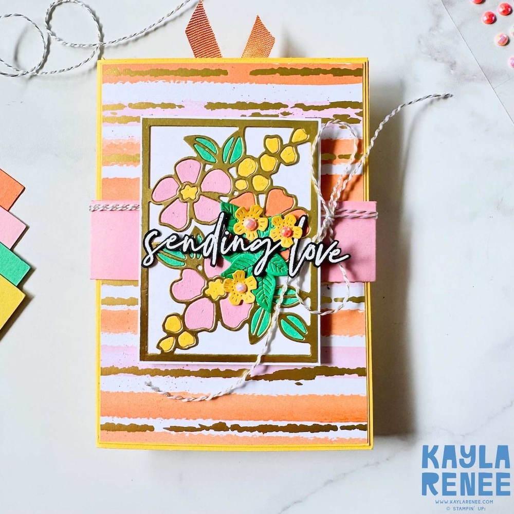 Front view of a pop out angled accordion fold card in warm yellow, peach and pink tones, decorated with floral die cuts, gold detailing and a “Sending love” sentiment.