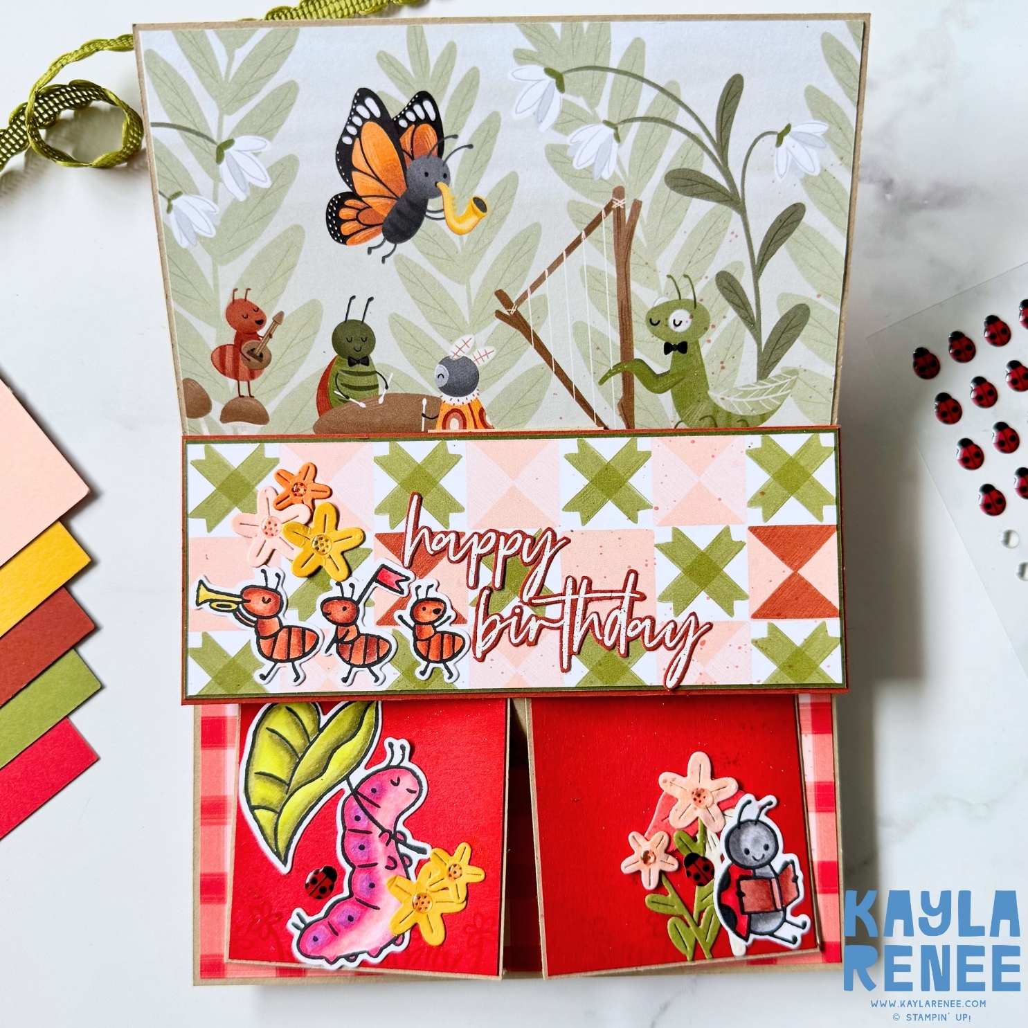 Full view of opened handmade birthday card with illustrated insects, musical grasshopper scene and layered “happy birthday” greeting across the centre panel.