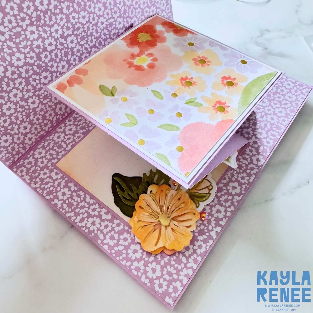 Expanding pop-up card partially opened showing layered floral patterned panels and dimensional flower embellishment inside.