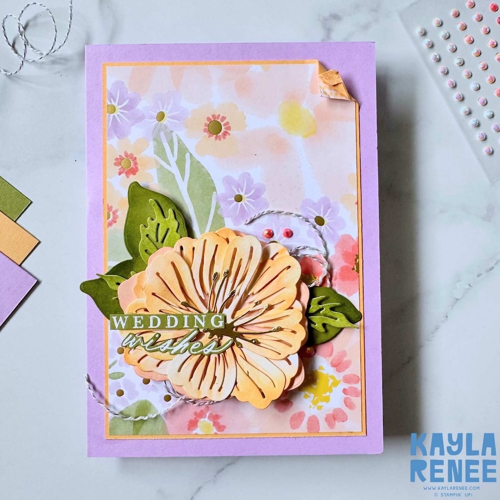 Front of handmade wedding card with layered peach die-cut flower, green leaves, twine accents and “Wedding Wishes” sentiment on soft floral patterned background.