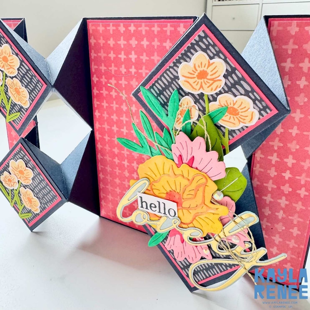 Angled view of dimensional floral cluster on a floating diamond pop-up card featuring yellow and pink flowers, green leaves, and layered “hello lovely” sentiment.