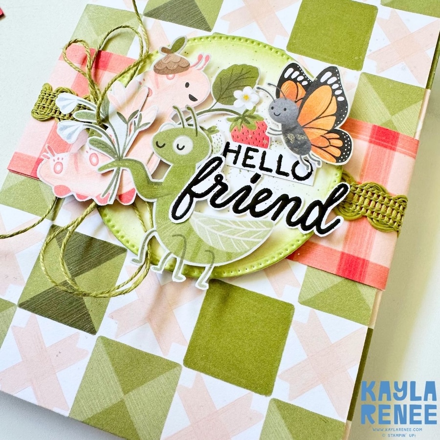 Angled close-up of Cute as a Bug mini album card showing dimensional layering, twine accents, stitched circle, and whimsical insect and floral elements.