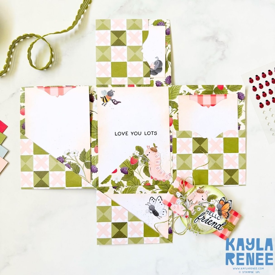 Fully opened mini album card displaying multiple panels and pockets for photos or journaling, featuring strawberries, bugs, and floral patterns with soft green and pink tones.