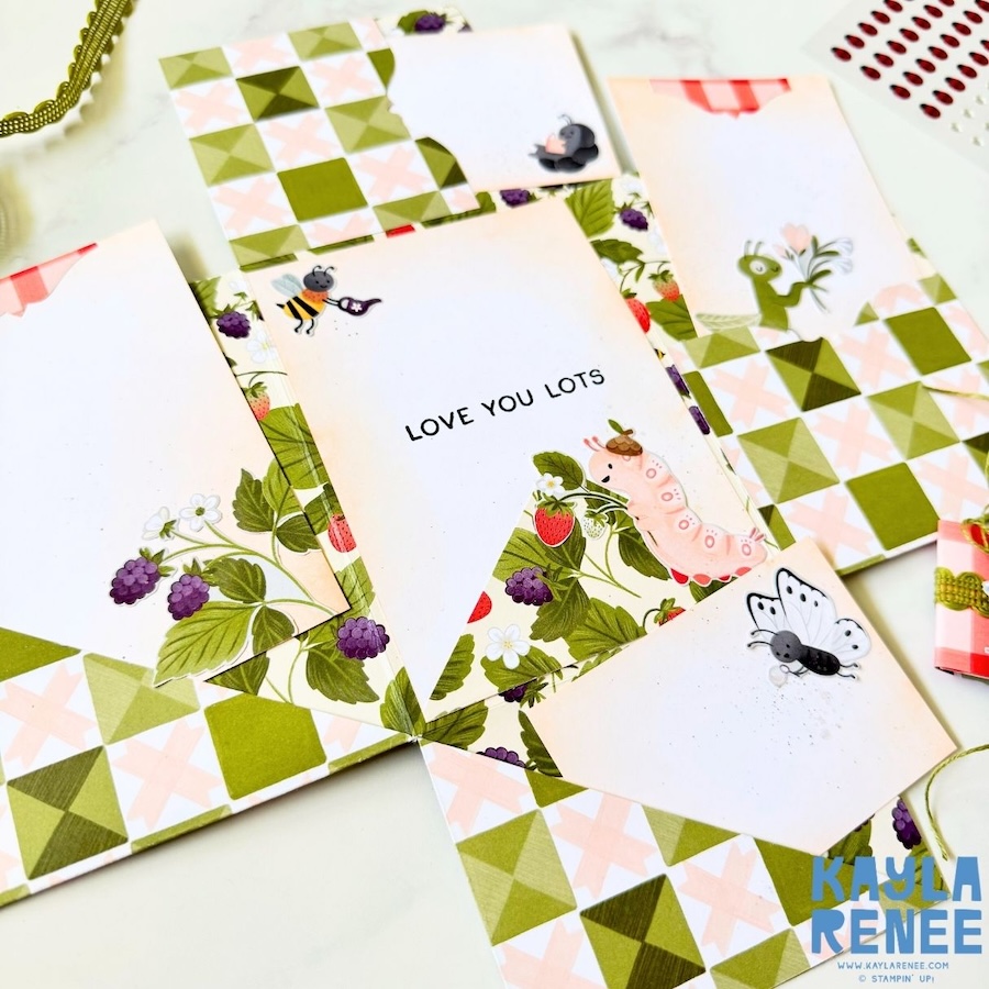 Close-up of mini album inserts featuring stamped bugs, strawberries, and florals with soft ink blending and journaling space inside the interactive card.