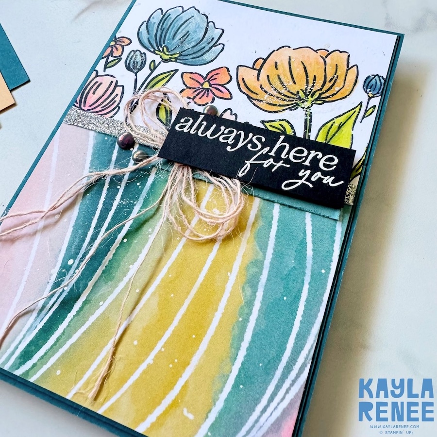 Angled detail of the card highlighting the dimensional layers, including the coloured flowers, textured designer paper, metallic accents, and natural twine bow clustered beneath the sentiment.