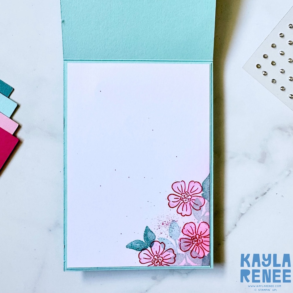 Inside view of the card featuring a clean white panel with stamped floral accents in the bottom corner in coordinating pink and aqua tones.