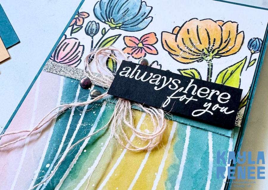 Close-up of a handmade card featuring hand-coloured floral images from the Stampin’ Up! Flowers Fair stamp set, paired with Painted Illusions Designer Series Paper in soft teal, yellow and pink tones, finished with a black sentiment strip reading “always here for you” and a twine bow.