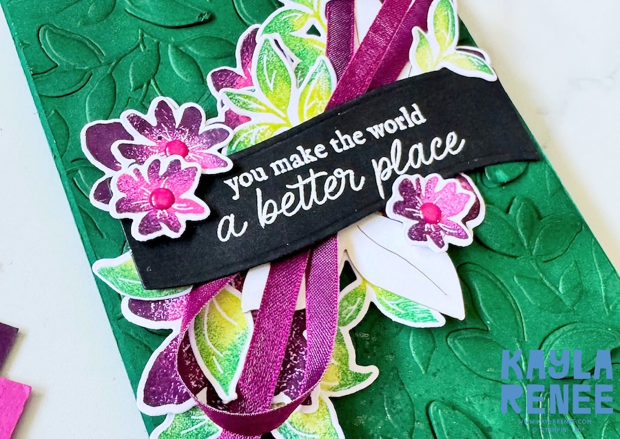Close-up of a handmade Stampin’ Up! Garden Poetry Suite card featuring layered pink and purple flowers, green leaves, and a black sentiment strip reading “you make the world a better place” on a deep green embossed background