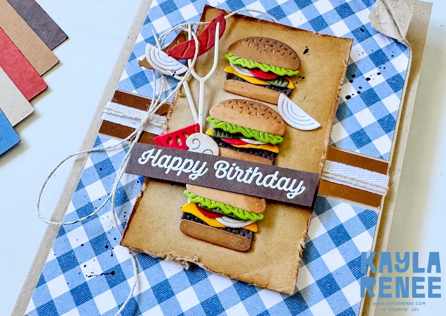 Close-up of handmade birthday card featuring layered burger die cuts from the Stampin’ Up! BBQ Master bundle on a distressed panel, with twine, grilling tool accents, and “Happy Birthday” sentiment over blue gingham paper.