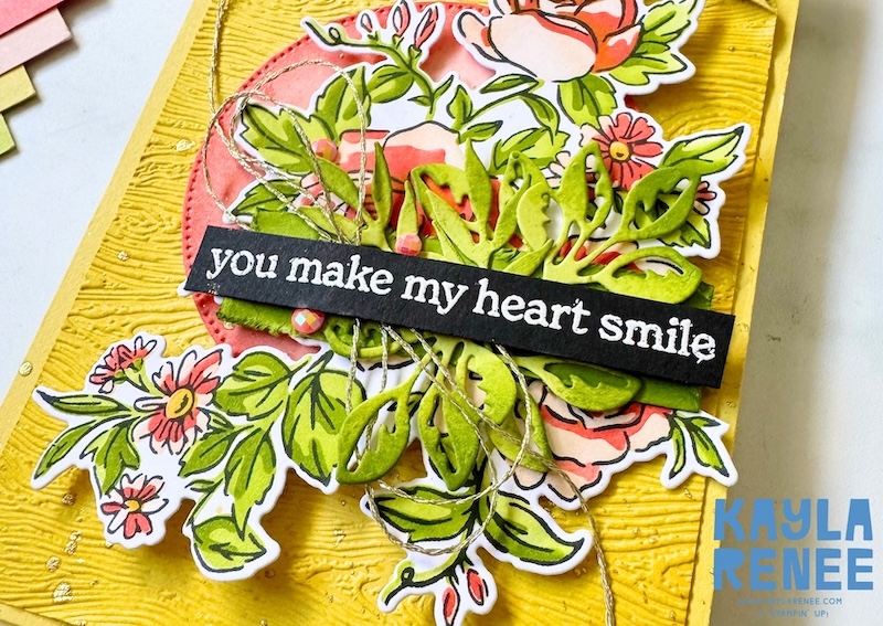 Close-up of a handmade card created with the Stampin’ Up! Layers of Beauty bundle, featuring layered floral images, die-cut greenery, gold thread accents, and the sentiment “you make my heart smile” on a textured yellow background.