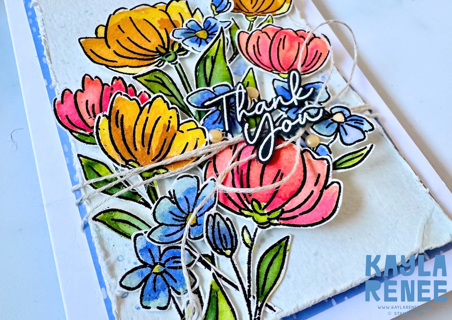 Detailed view of layered floral cluster with hand-painted watercolour effect, dimensional die cuts, and sentiment layered over rustic textured background.