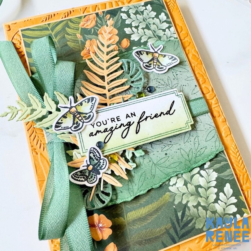 Angled close-up of a layered botanical card made with the Stampin’ Up! Moonlit Flora Suite, showcasing the new Golden Glow and Peaceful Pine Stampin’ Up! colours, detailed die-cut ferns, moth accents, soft green ribbon, and a friendship sentiment.