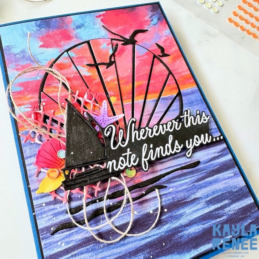 Angled close-up of a Stampin’ Up! Scenic Coast Suite card highlighting dimensional coastal layers, black die-cut sailboat and birds, twine accents, seashell embellishments, and a dramatic pink and blue sunset sky.