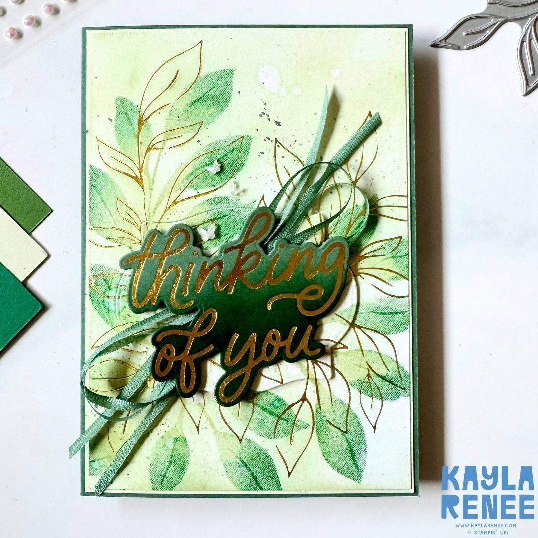 Handmade thinking of you card created using the Stampin’ Up! Botanical Glow and Classic Greetings hot foil products. The card features gold hot foiled botanical images layered over soft green ink blending, with a large gold foiled "Thinking of You" sentiment as the focal point. Finished with layered ribbon, delicate embellishments, ink splatter, and dimensional details for an elegant botanical design.