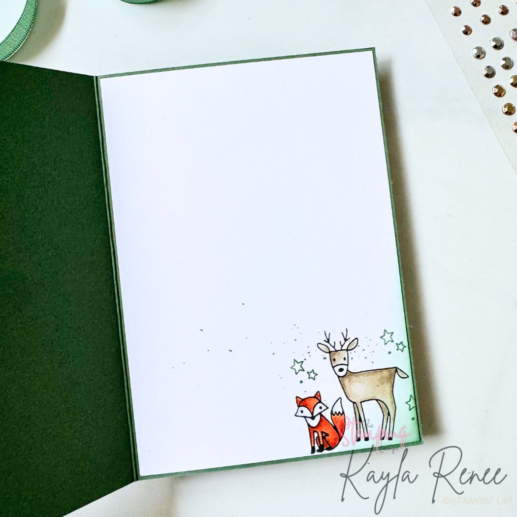 Inside of a handmade Christmas card featuring the Stampin’ Up! Woodland Wishes stamp set. The clean white writing panel is decorated with a hand-coloured deer and fox in the bottom corner, accented with stamped stars and subtle ink splatter to coordinate with the woodland-themed Christmas card front created for The Stamping Lounge Christmas in July event.