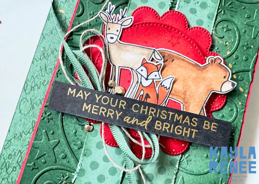Close-up of a handmade Christmas card created for The Stamping Lounge Christmas in July event using the Stampin’ Up! Woodland Wishes stamp set and Swirls of Magic Embossing Folder. A layered focal point features a hand-coloured deer, fox and bear in front of bright red stitched circles, finished with soft green ribbon, linen thread, gold embellishments and a gold heat-embossed "May Your Christmas Be Merry and Bright" sentiment.