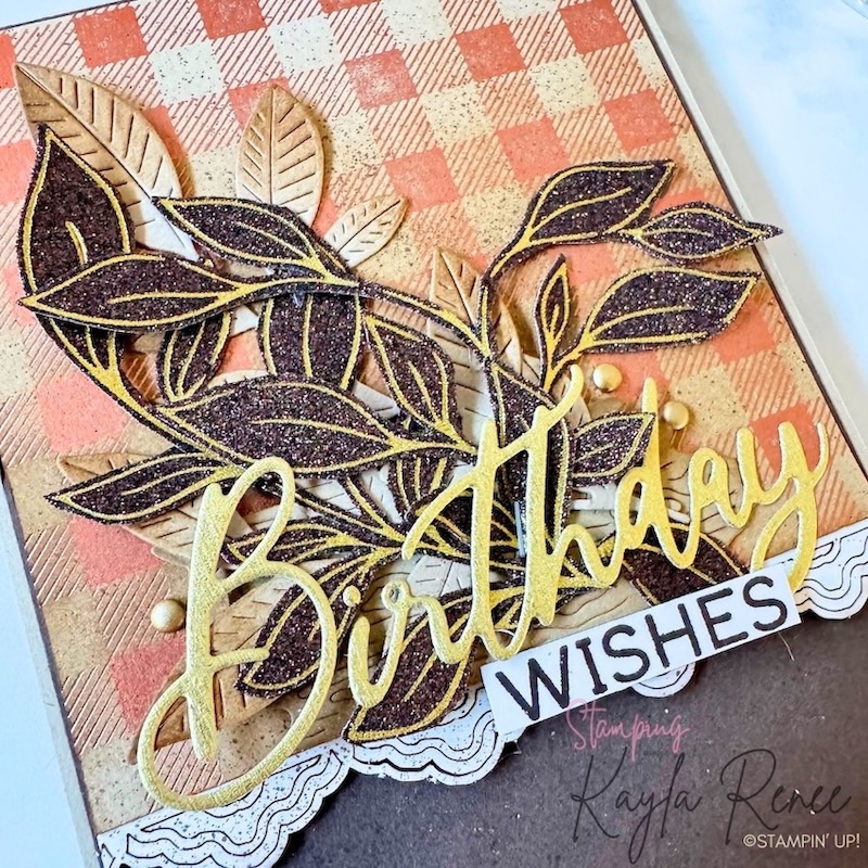 Close-up of a handmade birthday card featuring a neutral colour palette, layered dark foliage with gold hot foil accents, natural-toned leaves, textured patterned paper and a large gold “Birthday” sentiment with “Wishes” underneath.