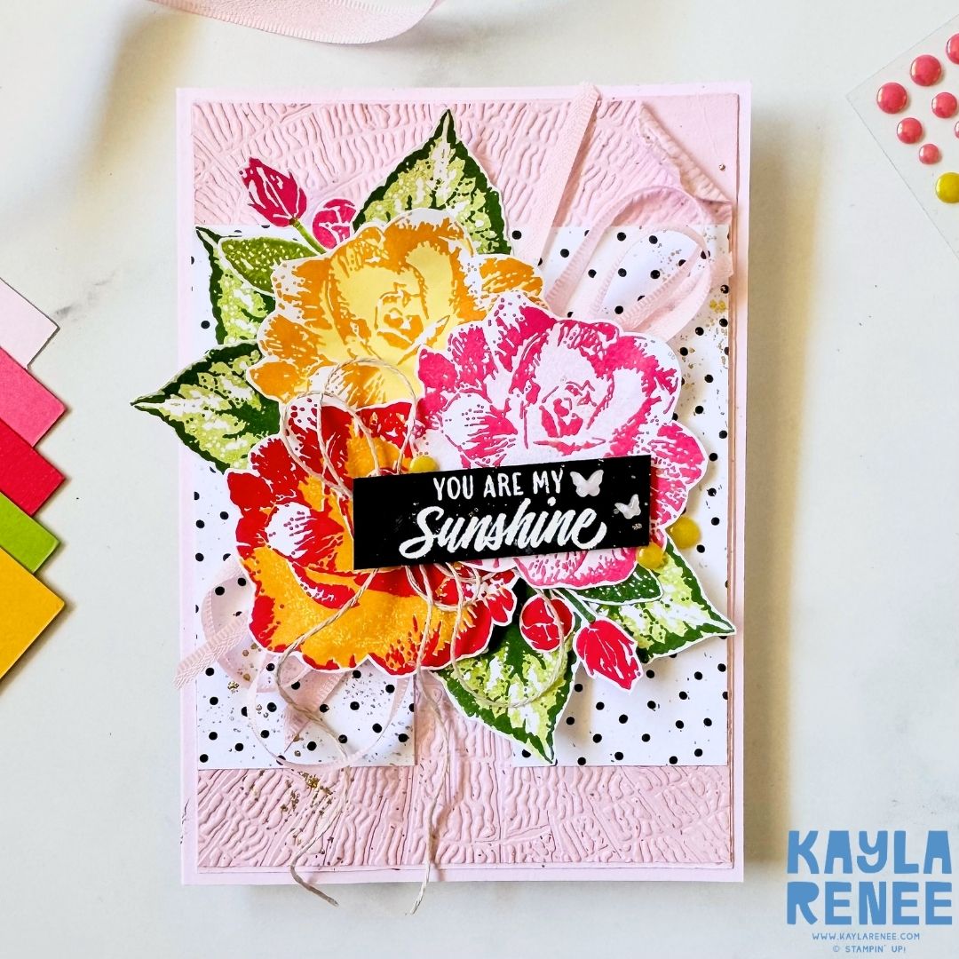 Handmade floral greeting card created using the Stampin’ Up! Begonia Belle stamp set, featuring layered yellow, orange, pink and red flowers with green leaves on a soft pink textured background. A black sentiment panel reads “You are my Sunshine,” with ribbon, twine and embellishments adding texture and dimension.