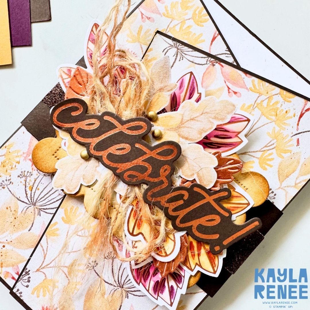 Close-up of an angled gatefold card decorated with autumnal patterned paper, layered flowers and leaves, natural twine and copper hot foil accents. The raised “Celebrate!” sentiment is the focal point.