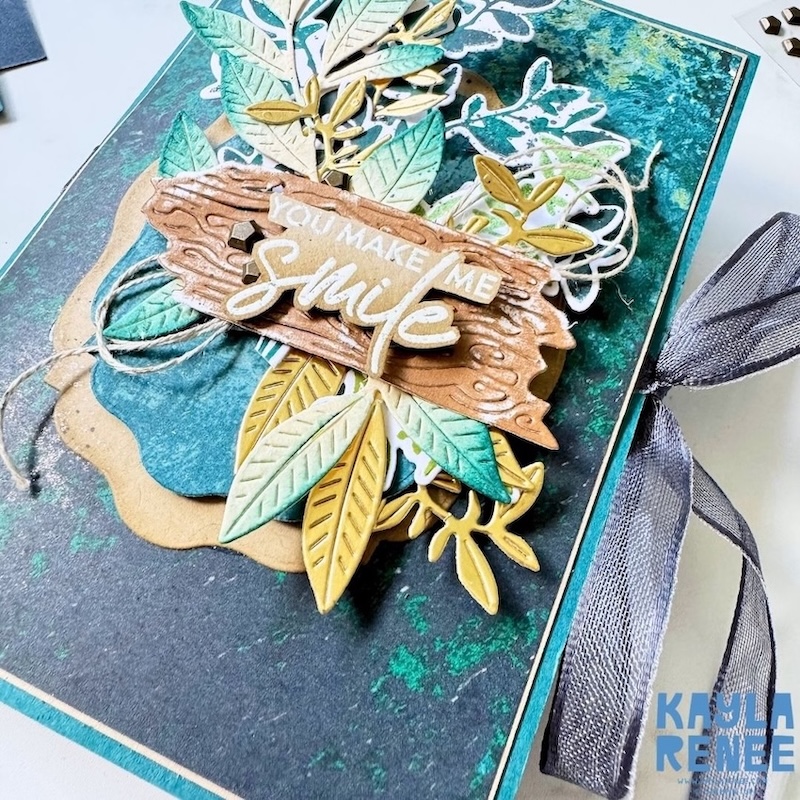 Close-up of a handmade pop-up expanding pocket card showing layered embossed leaves, gold foliage, botanical elements and a textured wood-effect “You Make Me Smile” sentiment.