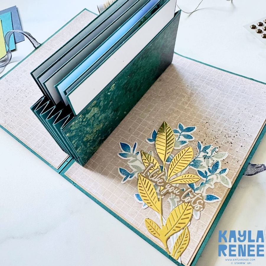 Open view of a pop-up expanding pocket card showing the dimensional accordion mechanism, expanding pocket and decorated interior panel with gold and blue foliage and a “I like you lots” sentiment.