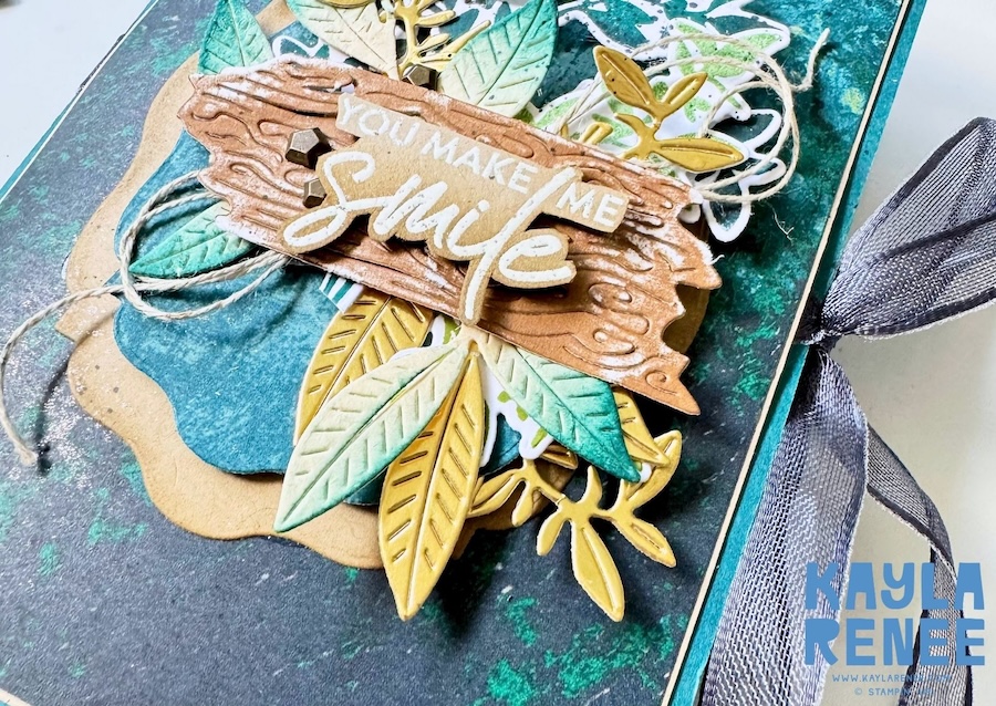 Front of a handmade pop-up expanding pocket card featuring the Stampin’ Up! Nature Walk Suite in teal, green, blue and gold, with layered foliage, a wood-textured sentiment panel reading “You Make Me Smile” and a large ribbon bow.