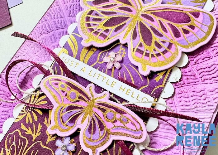 Close-up of a handmade purple and gold card created using the Stampin’ Up! Hot Foil System, Garden Silhouette hot foil dies and Butterfly Flight hot foil dies. Two layered butterflies feature intricate gold hot foil detailing over purple backgrounds, with coordinating gold-foiled floral imagery, ribbon, linen thread and small purple flower embellishments. The card features a “Just a Little Hello” sentiment.