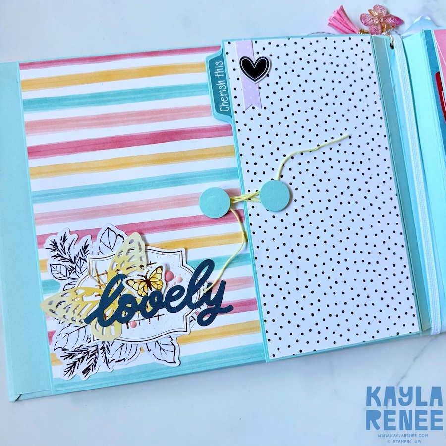 Mini album page featuring pastel striped paper, a black-and-white polka dot pocket with a heart closure, and layered floral and butterfly embellishments surrounding a “lovely” sentiment.