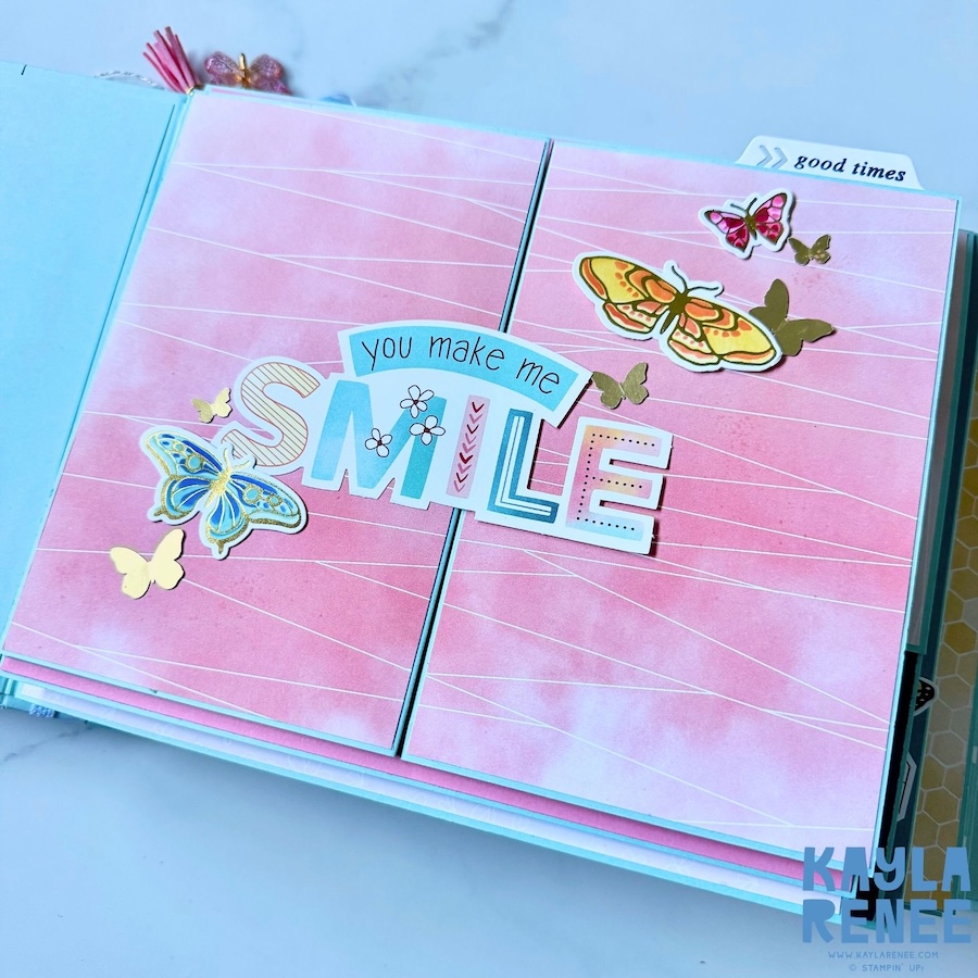 Open view of the handmade Stampin’ Up! mini album featuring a large pink “you make me SMILE” scrapbook page decorated with colourful butterflies, alongside a journaling area on a light aqua background.