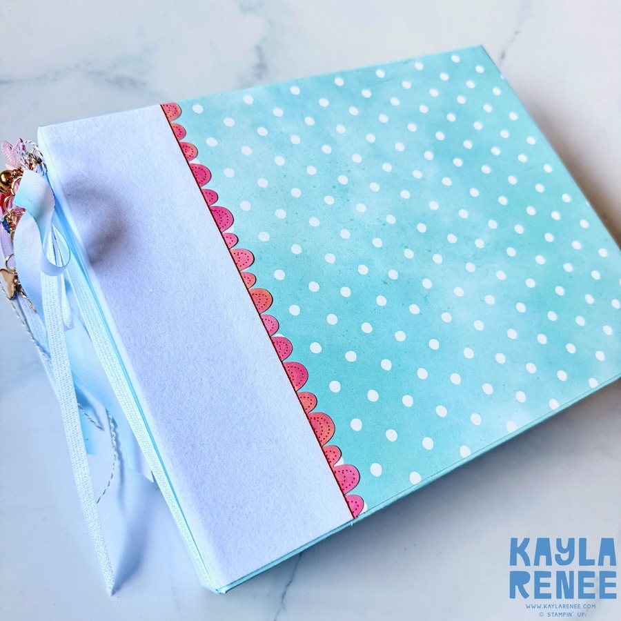 Close-up of the handmade mini album cover decorated with light aqua and white polka dot paper, a pink scalloped border and layered patterned paper details.