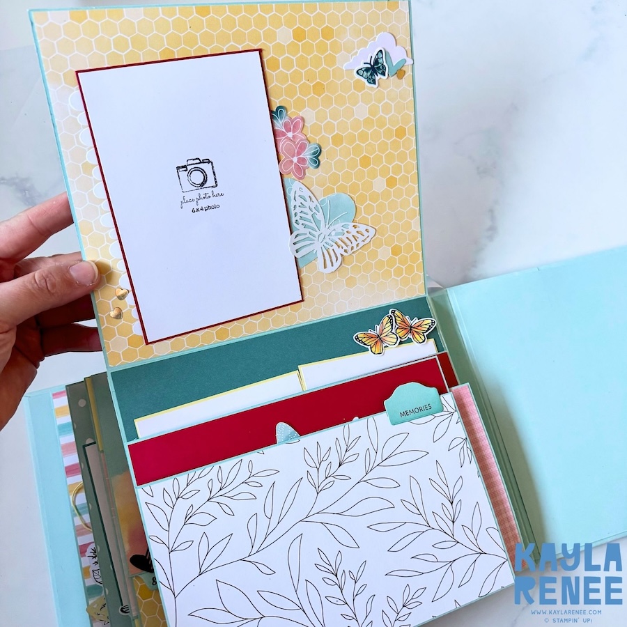 Mini album page featuring a large 6-by-4-inch photo mat on yellow honeycomb-patterned paper, with layered butterfly and floral embellishments and additional journaling and memory cards tucked into a pocket below.