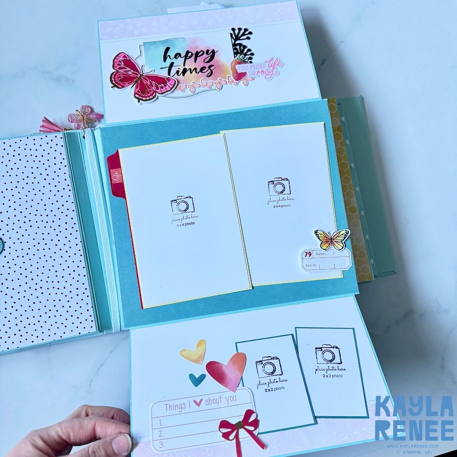 Detailed mini album spread featuring two photo mats, colourful butterfly embellishments, layered labels and decorative hearts on a bright pink background.