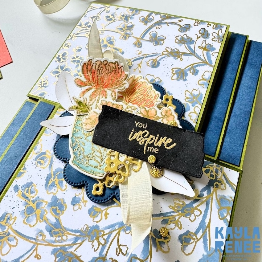 Detailed view of the double flip book card showing layered floral elements, a decorative vase, gold die-cut accents and the “You inspire me” sentiment against blue and gold patterned paper.